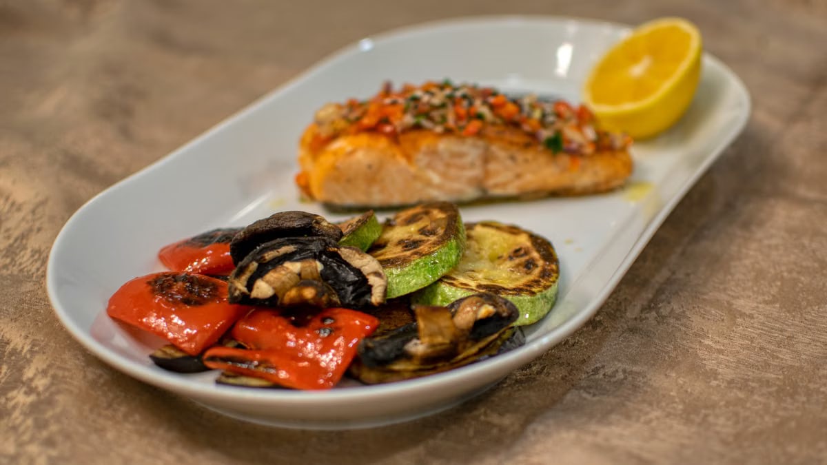 A delicious grilled salmon fillet with roasted vegetables served on a white plate.